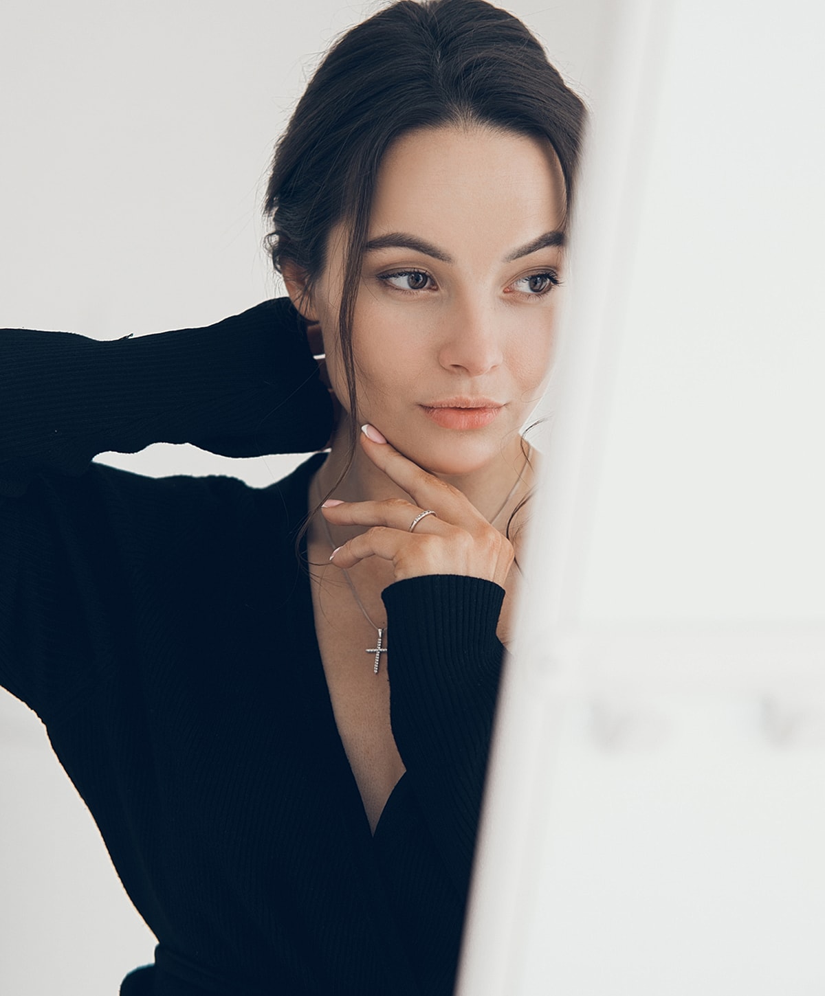 Woman in black sweater, thoughtful expression, near mirror.