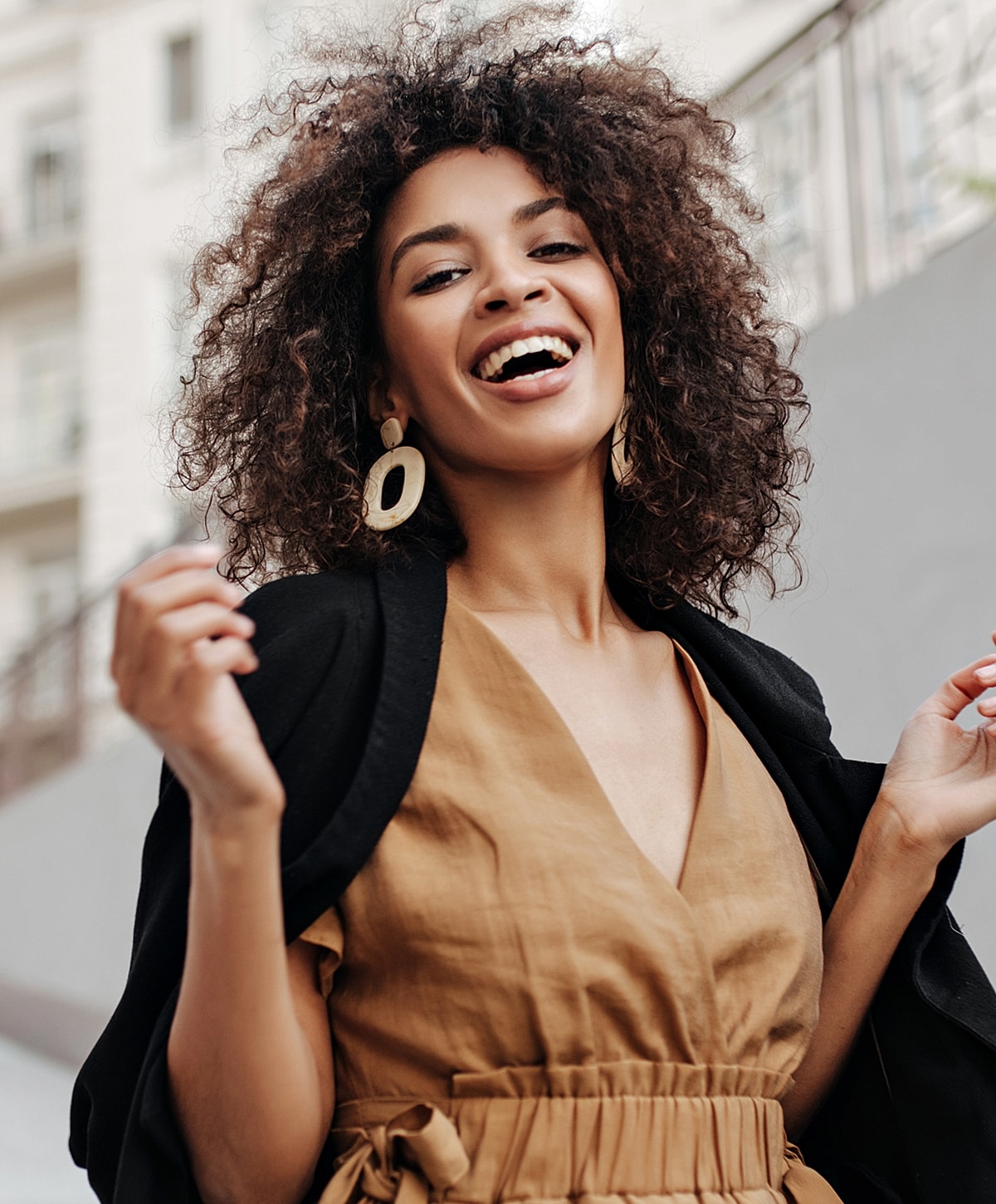 Smiling woman with curly hair in urban setting.
